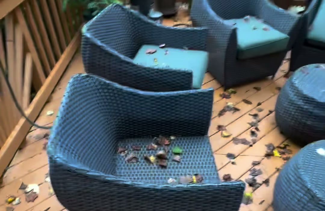 A wicker patio set spread across a timber deck, leaves on the boards, waiting to be taken away.