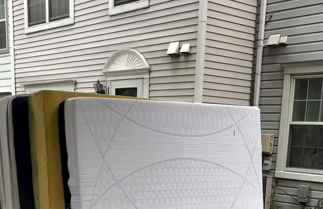 A mattress and box springs leaning against the siding of a house, waiting for collection.