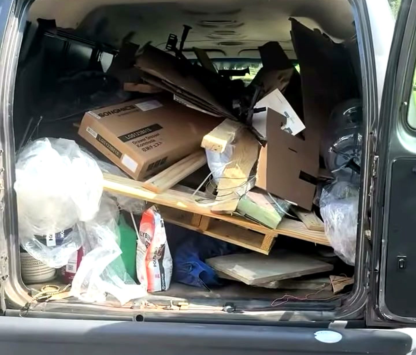 The back of the Bin Movers van with the rear doors open, packed to the roof with flattened boxes, a pallet, timber offcuts and bagged junk.