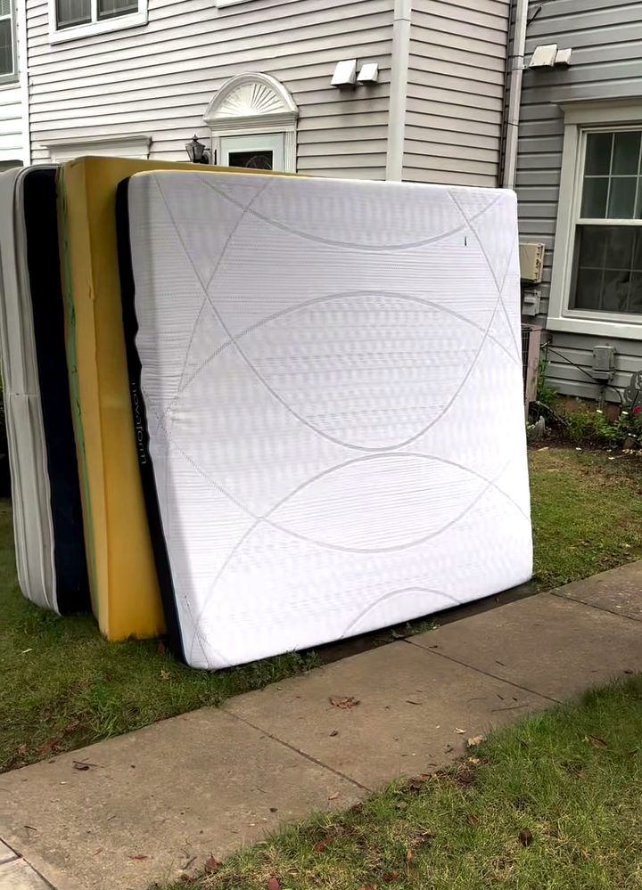 Two box springs and a mattress leaning against the side of a house, put out for collection.